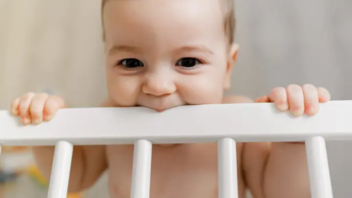 A cute teething baby chewing on the crib bar